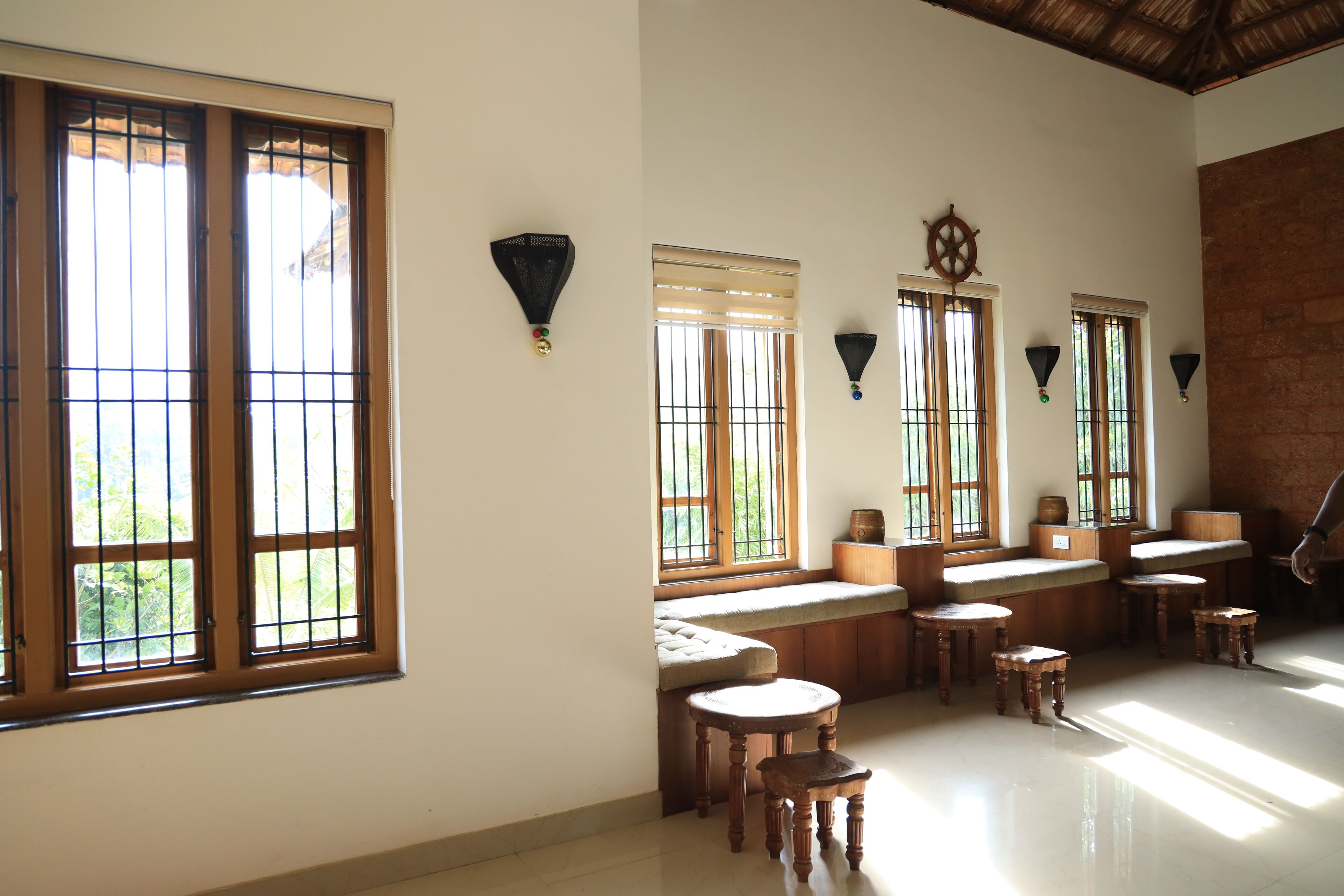A room with large windows, wooden benches, and small stools.