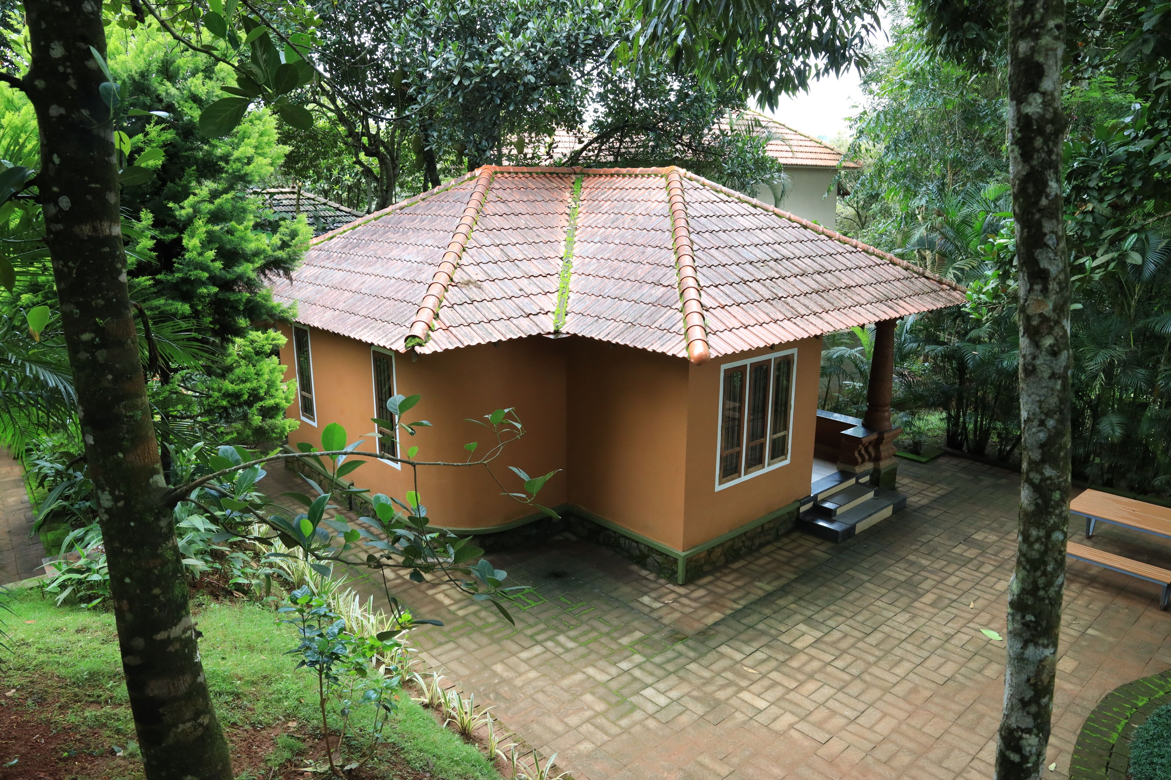 A small, single-story building with a tiled roof, surrounded by lush greenery and trees.
