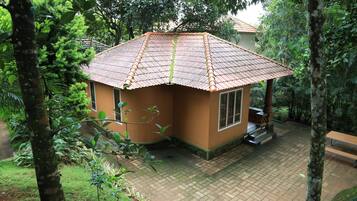 A small, single-story building with a tiled roof, surrounded by lush greenery and trees.