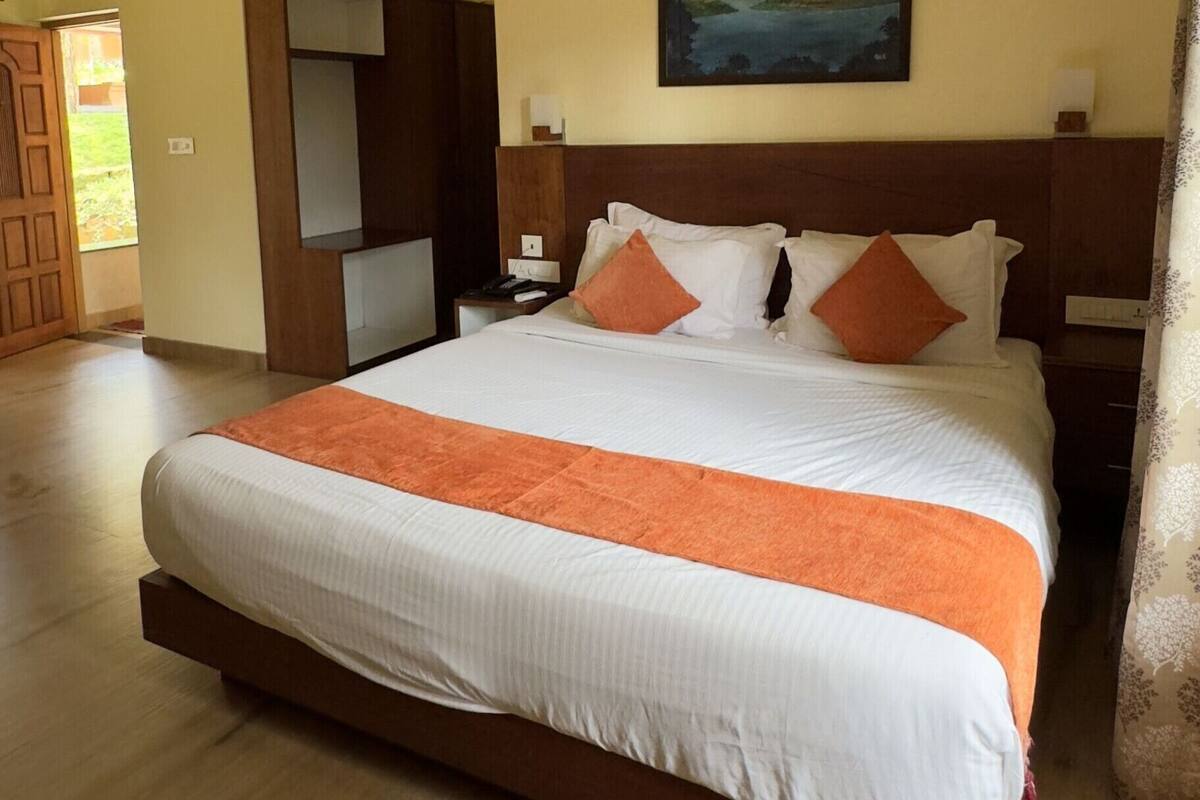 A hotel room with a large bed, a wooden headboard, a painting on the wall, and a wooden chair.