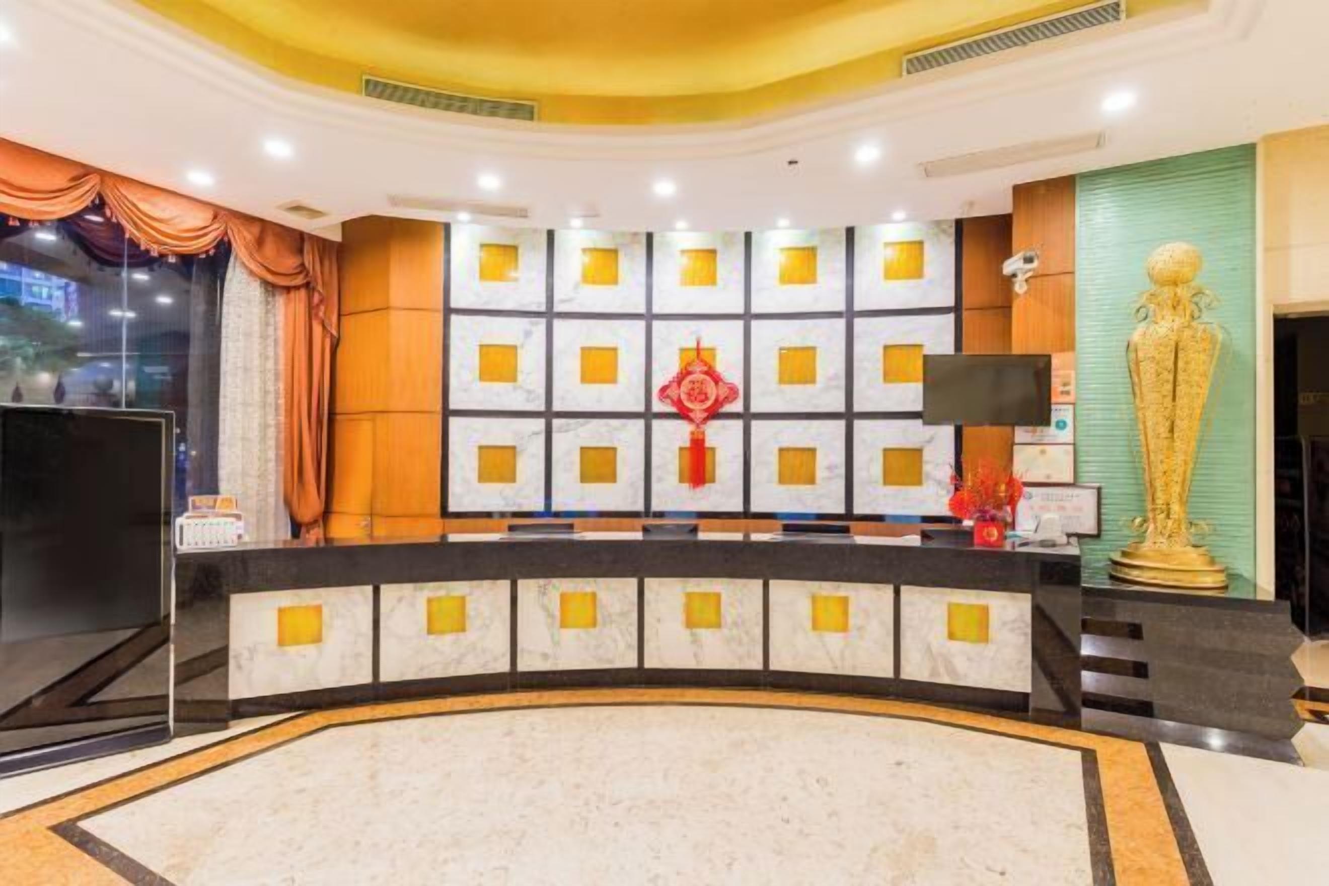 Una zona reception di un hotel con una scrivania a forma di curva, un grande schermo televisivo e una statua decorativa dorata.