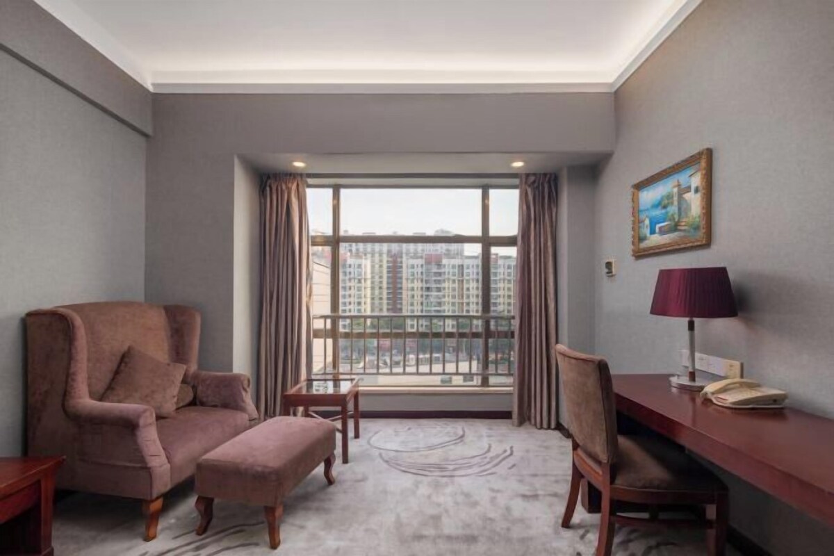 A hotel room with a large window, a sofa, a desk, and a chair.