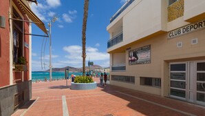 A brick-paved walkway with a palm tree planter, a building with a 'CLUB DEPORTIVO FRANCO' sign, and a view of the sea.