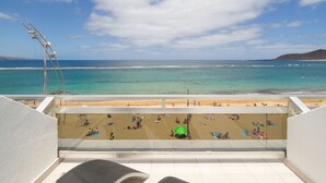 A beach view from a balcony with a clear sky, calm sea, and people sunbathing.