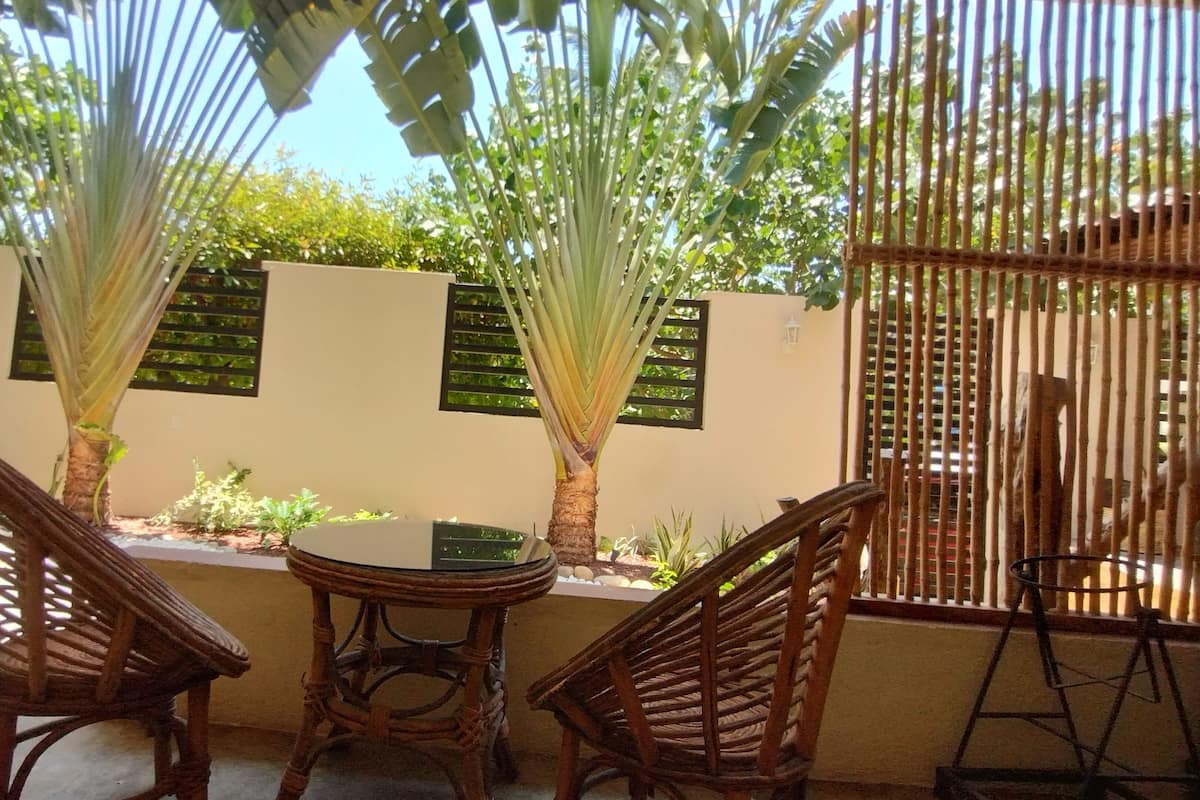 Eine Terrasse mit zwei Korbstühlen, einem runden Tisch und einem kleinen Topfpflanzen.