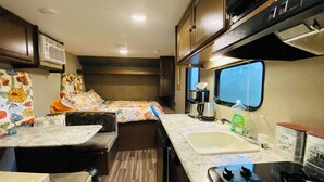 A compact RV kitchen with a stove, sink, and two sleeping areas with colorful bedding. - HideOut in The Highlands 
15min from Skyline Trail
Walking distance from Sunsets (Pleasant Bay)