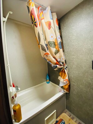 Et badeværelse med badekar, bruseforhæng med blomstermønster og en håndholdt bruser samt en shampoo-flaske.