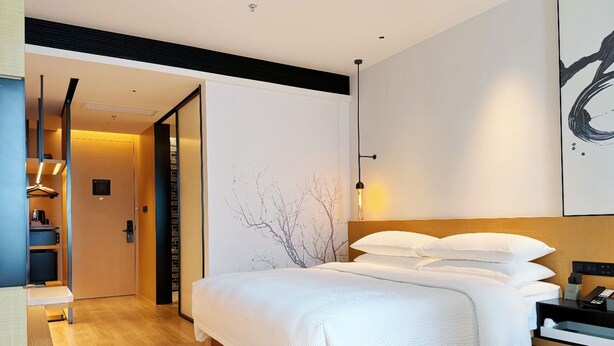 Een moderne hotelkamer met een groot bed, een houten vloer, een kledingkast en een bureau met stoel.