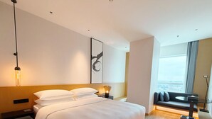 Een moderne hotelkamer met een groot bed, uitzicht op de stad, een bank en een minimalistisch design.