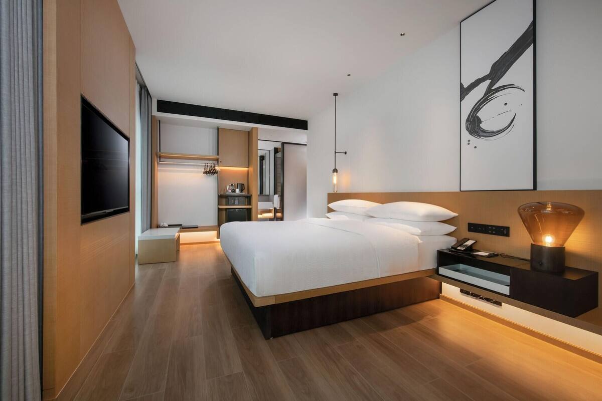 A modern hotel room with a large bed, bedside tables, a flat-screen TV, and a wall-mounted artwork.