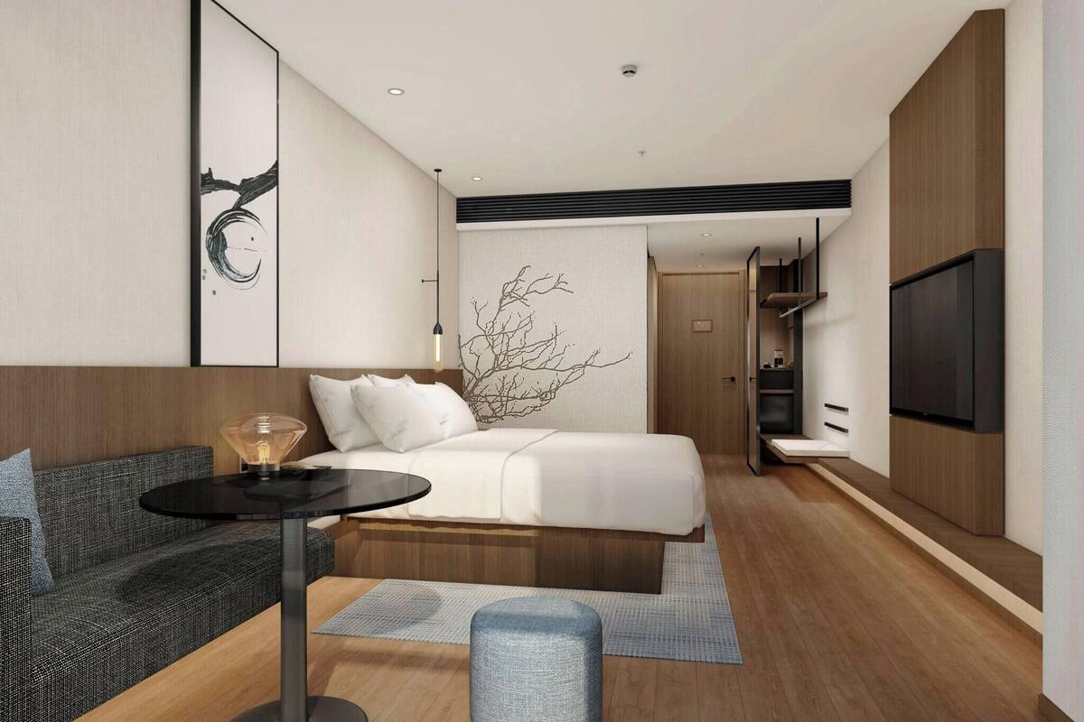 A modern hotel room with a bed, a sofa, a small table, and a TV.