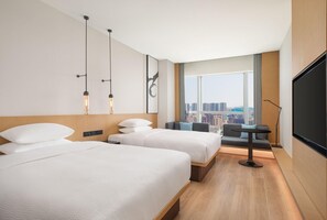 Une chambre d’hôtel avec deux lits, une vue sur la ville, une grande fenêtre et un téléviseur à écran plat.