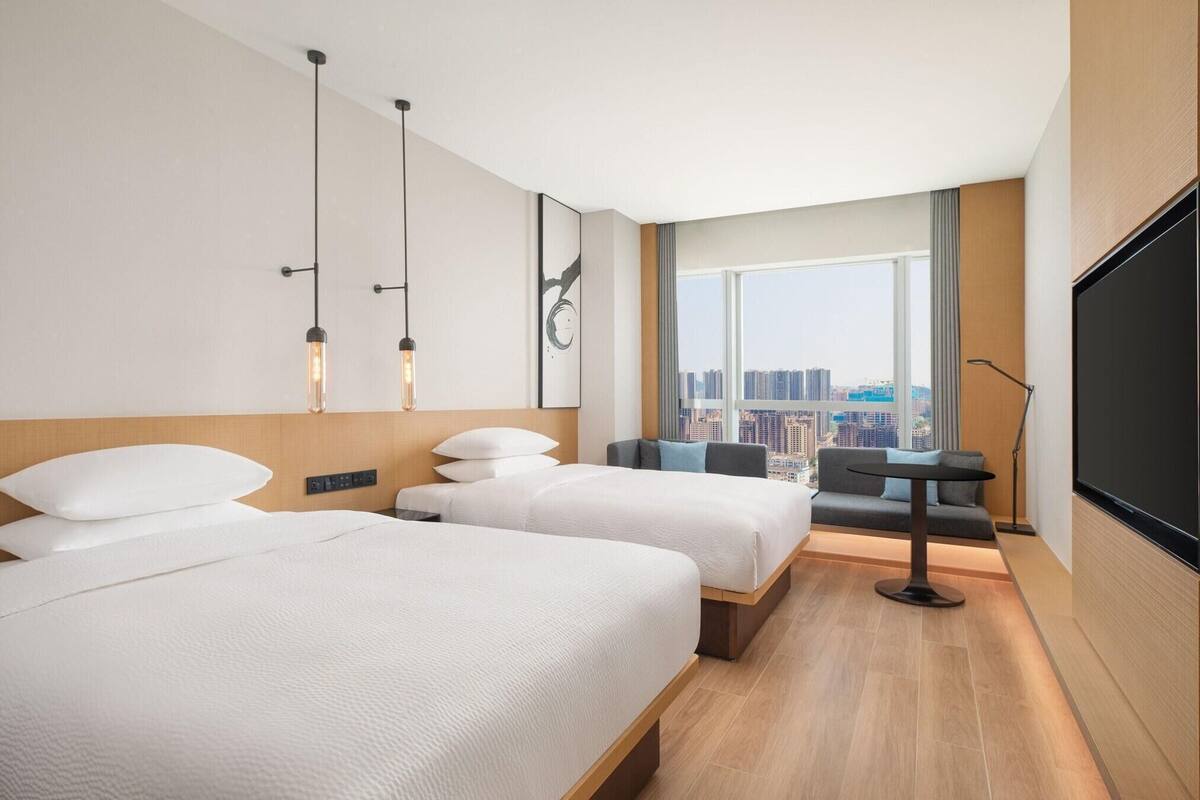 A hotel room with two beds, a city view, a large window, and a flat-screen TV.