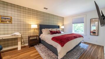 Un dormitorio con cama, mesitas de noche, escritorio, silla, ventana con persianas y un espejo en la pared.