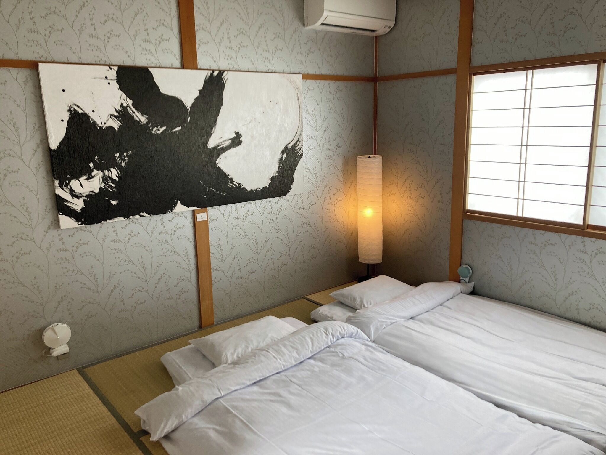 A room with a bed, a wall-mounted air conditioner, a lamp, and a window with a view.