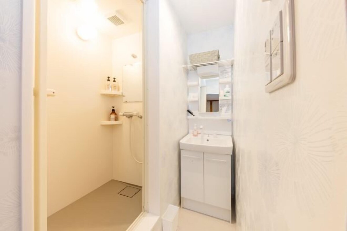 A narrow bathroom with a shower, a sink, and a mirror.