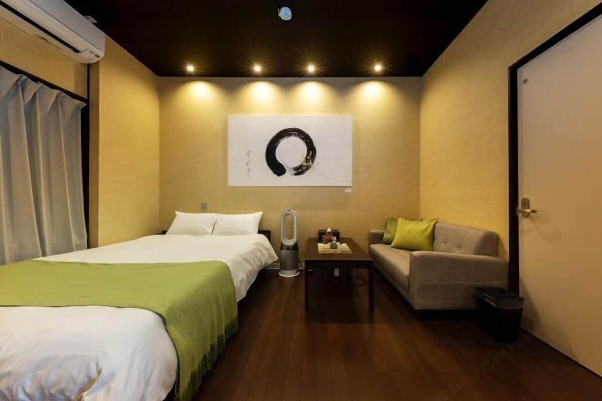 A hotel room with a bed, a sofa, a small table, and a wall-mounted artwork.