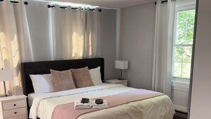 Un dormitorio ordenado con una cama grande, mesitas de noche y una ventana con cortinas.