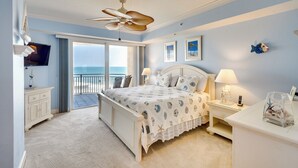 A bedroom with a bed, a nightstand, a dresser, a ceiling fan, a TV, and a view of the ocean. - Daytona Beach Condo: Pool Access, Oceanfront (Daytona Beach Shores)