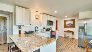 Una cocina con armarios blancos, encimera de granito, refrigerador de acero inoxidable y suelo de madera.