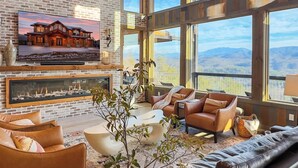 Un salon spacieux doté d’une cheminée, de canapés en cuir et de grandes fenêtres offrant une vue sur les montagnes.