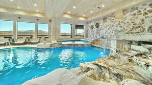 Une piscine intérieure avec vue sur les montagnes, des murs en pierre et un plafond en bois.