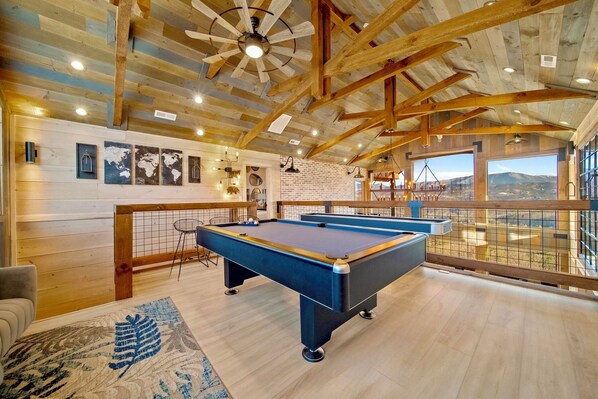 A pool table in a room with wooden beams and a view of a mountain.