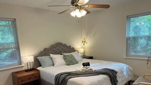 Een slaapkamer met een bed, nachtkastje, lamp, plafondventilator en een raam met zonwering.