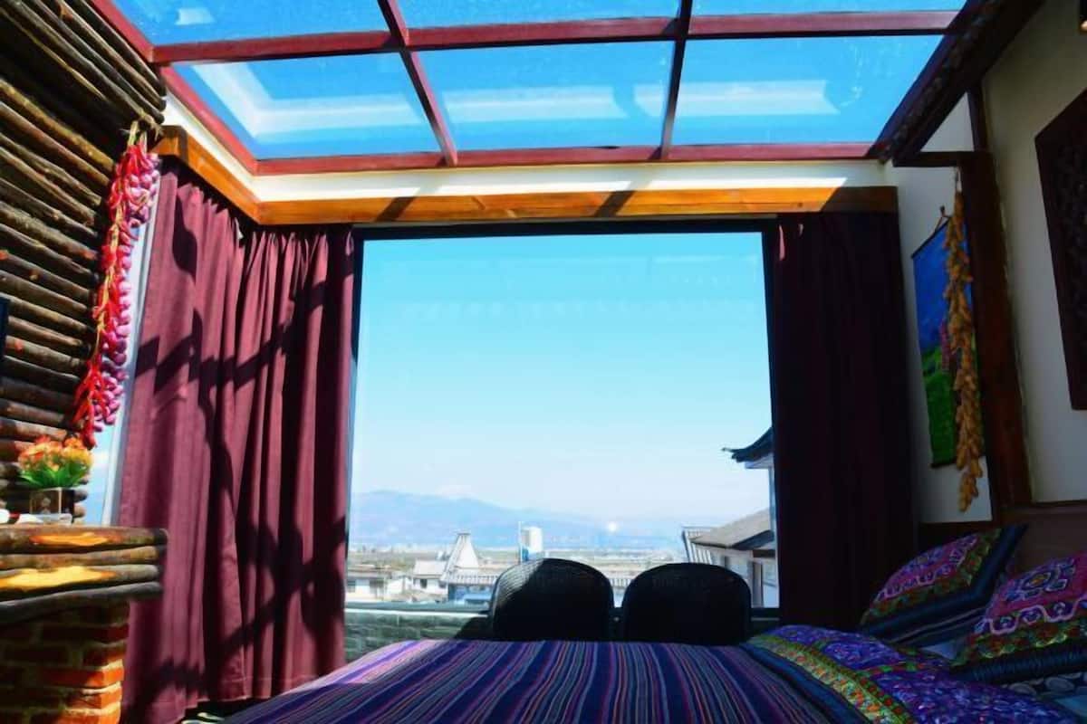 A room with a large skylight, a bed with colorful bedding, and a view of the cityscape.