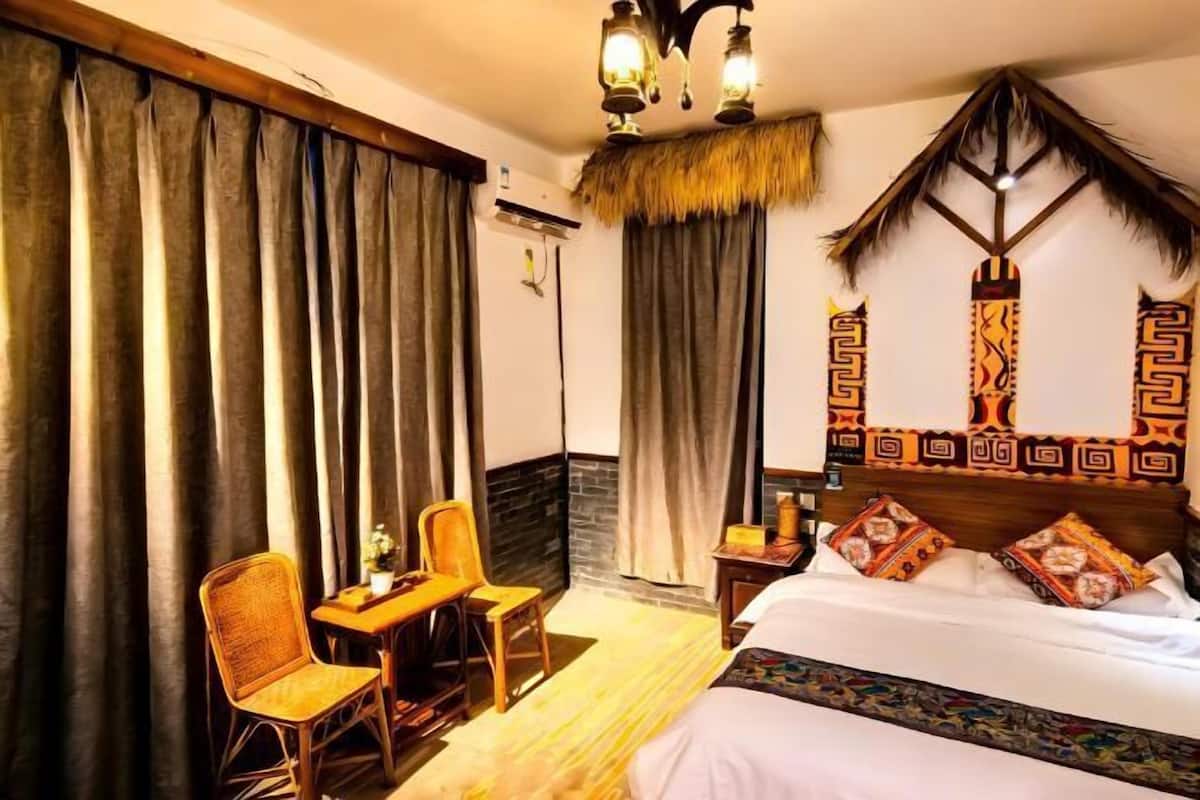 A hotel room with a bed, two chairs, a table, a decorative wall, and a ceiling light fixture.