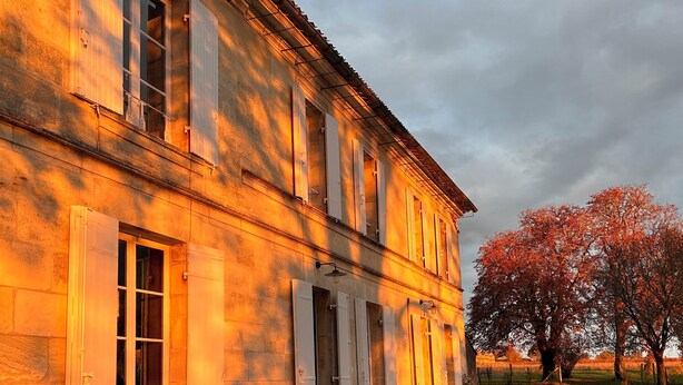 A building with a gravel driveway, potted plants, and a tree with red leaves. - Maison de Charme Pour Événements Familiaux ou Professionnels Domaine Le Pinquat (La Lande-de-Fronsac)