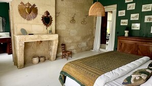 A bedroom with a bed, a small table, a chair, and a wall with pictures. - Maison de Charme Pour Événements Familiaux ou Professionnels Domaine Le Pinquat (La Lande-de-Fronsac)