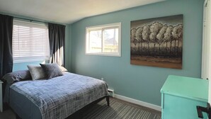 A bedroom with a bed, a window, a painting, and a teal cabinet. - Little Blue on Second St! Cozy & close to the beach, pub, bar, and downtown! (Port Stanley)