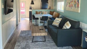 A modern living room with a dark blue sofa, a coffee table, and a TV mounted on the wall. - Little Blue on Second St! Cozy & close to the beach, pub, bar, and downtown! (Port Stanley)