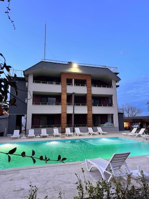 A multi-story hotel with a swimming pool, lounge chairs, and a balcony.