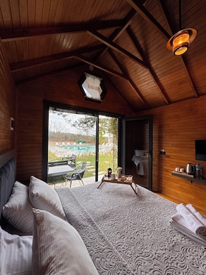 A bedroom with a large bed, a view of a pool, and a wooden ceiling.