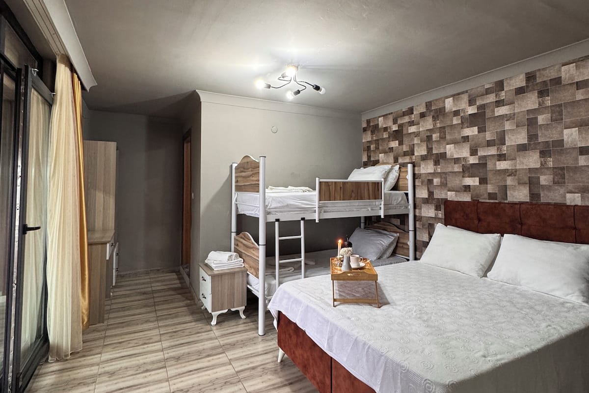 Une chambre avec un lit superposé, une table de chevet avec une lampe et une tête de lit ornée d’un motif géométrique.