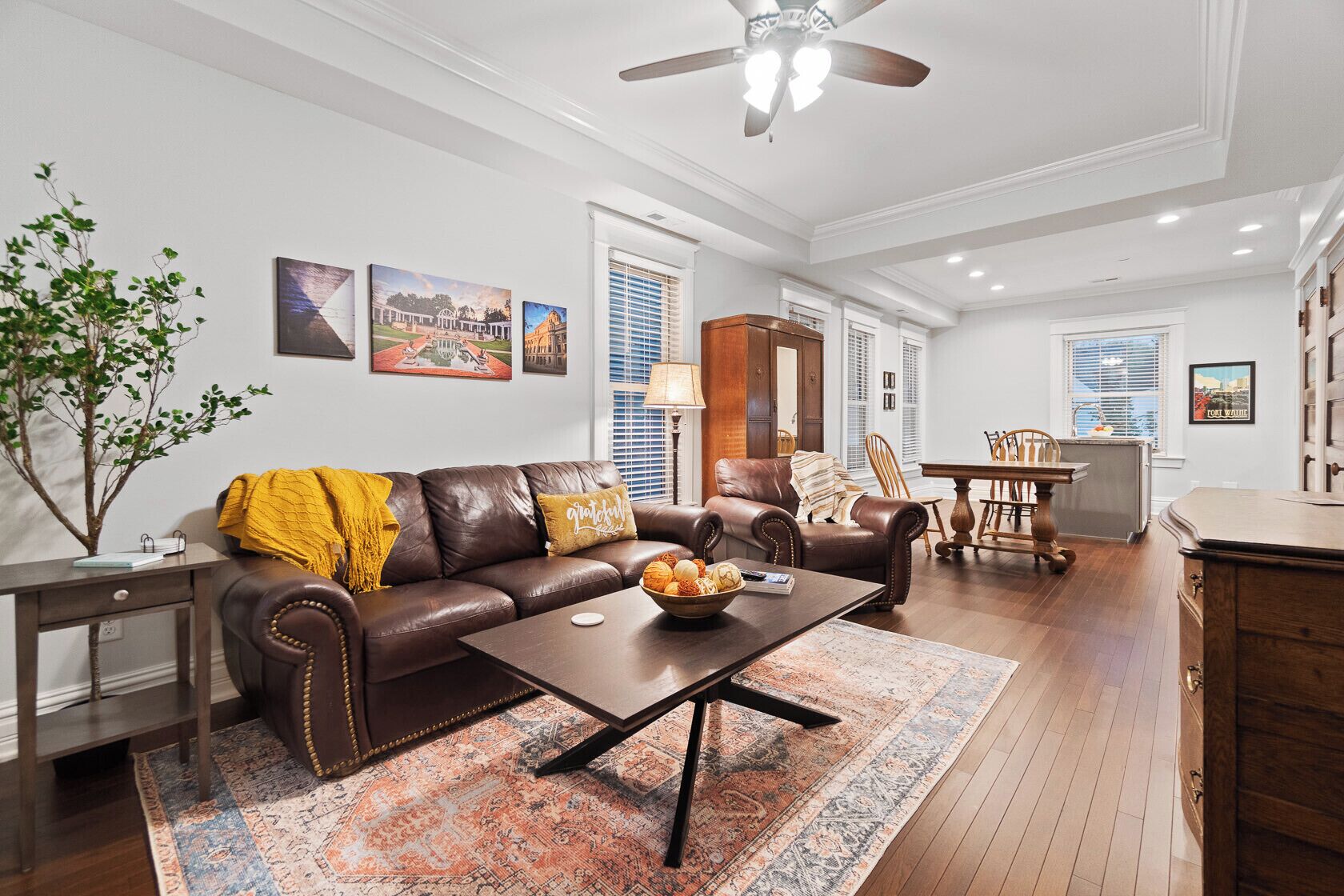 A spacious living room with a brown leather sofa, a coffee table, and a dining area with a wooden table and chairs.
