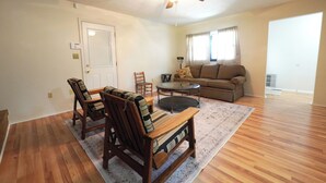 A spacious living room with hardwood flooring, a ceiling fan, a brown sofa, a coffee table, and two armchairs. - Spacious Home Near WEC, The Roberts Center and Wilmington College (Wilmington)