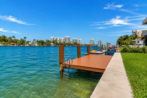 A waterfront dock with a concrete walkway, clear blue water, and a city skyline in the background.