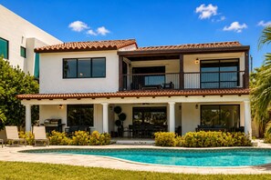 A two-story house with a swimming pool, outdoor seating, and a balcony.