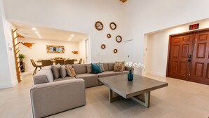 A modern living room with a sectional sofa, a coffee table, and a dining area in the background.