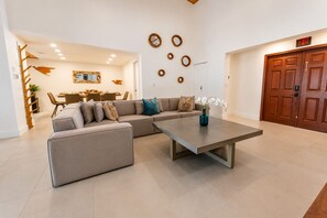 A modern living room with a sectional sofa, a coffee table, and a dining area in the background. - Española Bayfront Villa – North Bay Village Luxury (North Bay Village)