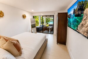 A bedroom with a bed, a wardrobe, a television, and a view of a balcony with outdoor furniture.