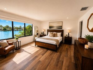 A bedroom with a large window, a bed, a nightstand, a dresser, and a mirror.
