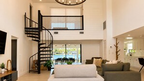 A spacious living area with a modern staircase, a dining area with a view, and a kitchen with white cabinets.