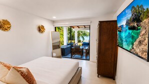 A bedroom with a bed, a wardrobe, a large window, and a view of an outdoor seating area.