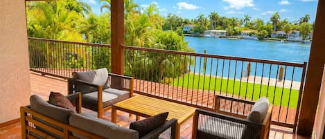 A covered outdoor seating area with a view of a lake and palm trees.