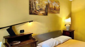 A hotel room with a bed, a desk with a lamp, a nightstand with a lamp, and two paintings on the wall. - Double room with single beds - Zudinì (Sternatia)
