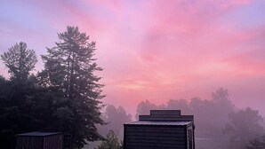 Une cabane rustique avec un toit en pente, entourée d’un champ herbeux et d’une forêt dense.